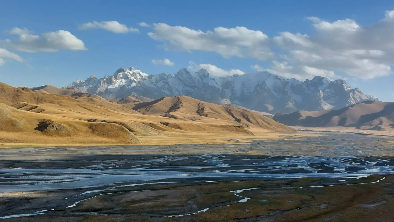 Paesaggio montano e fluviale in Asia Centrale con montagne innevate sullo sfondo.