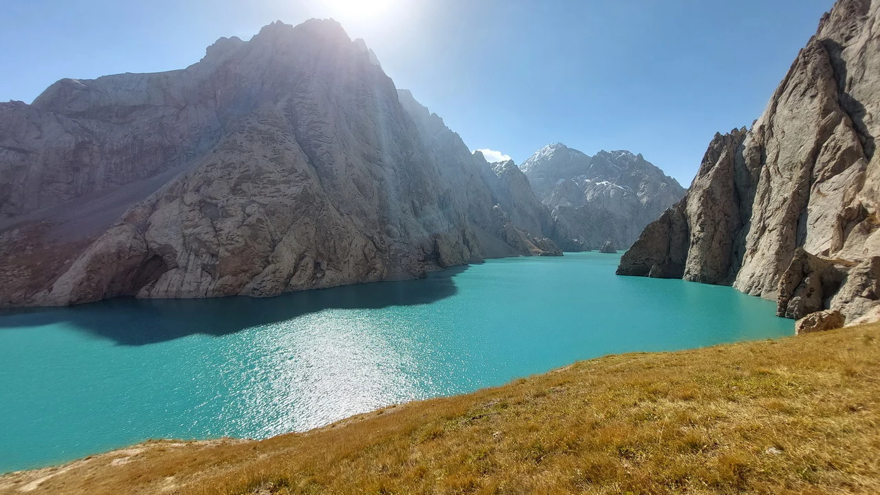 Un lago turchese si estende tra montagne rocciose in un paesaggio asiatico centrale.