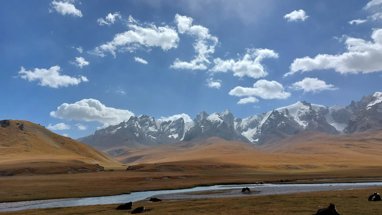 Un lago alpino si staglia tra montagne innevate e un paesaggio di praterie dorate.
