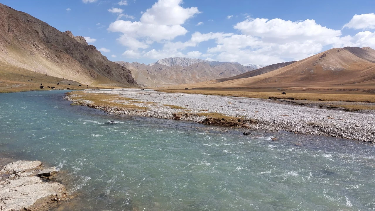 Un fiume turchese scorre attraverso un paesaggio montano arido in Asia Centrale.