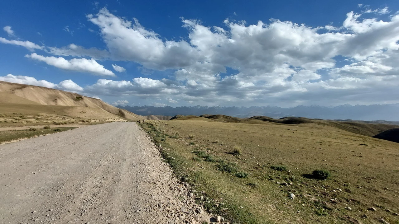 Una strada sterrata attraversa un paesaggio collinare in Asia Centrale sotto un cielo nuvoloso.