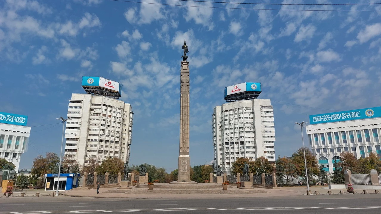 Il monumento all'Indipendenza ad Almaty è visibile in primo piano con edifici circostanti.