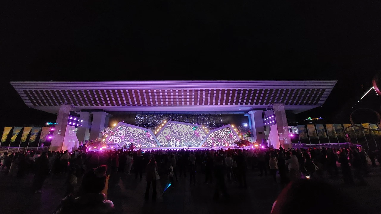 Una folla di persone si raduna davanti a un'ampia struttura architettonica illuminata di notte.