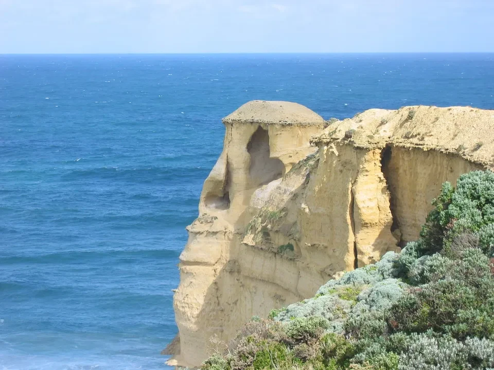 Scogliere costiere gialle e rocciose si affacciano sul vasto oceano sotto un cielo limpido.