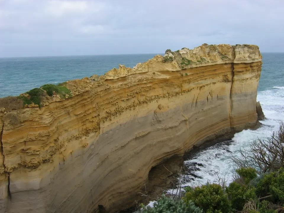 Una grande scogliera stratificata color ocra incontra l'oceano sotto un cielo coperto.