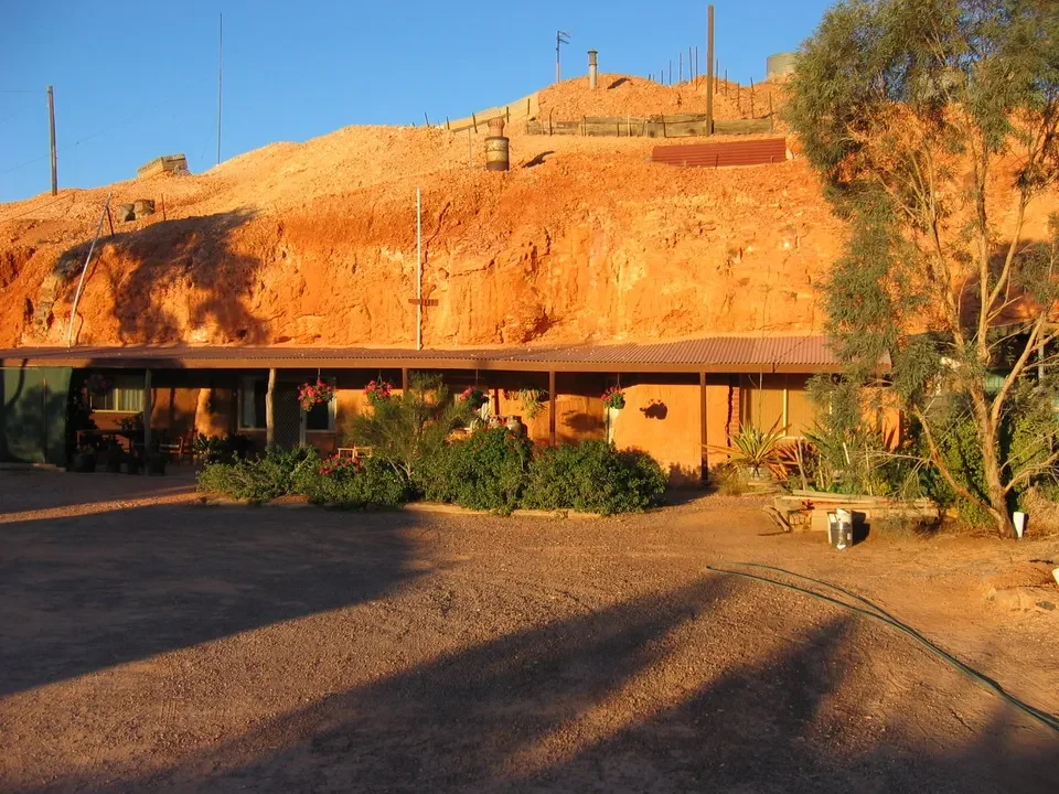 Paesaggio arido dell'Australia con una casa in terra rossa sotto il sole.