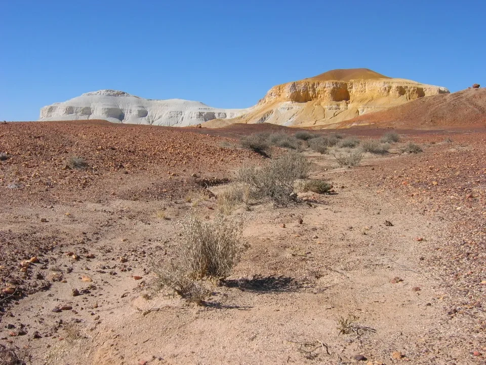 Paesaggio arido australiano con formazioni rocciose chiare sotto un cielo azzurro.