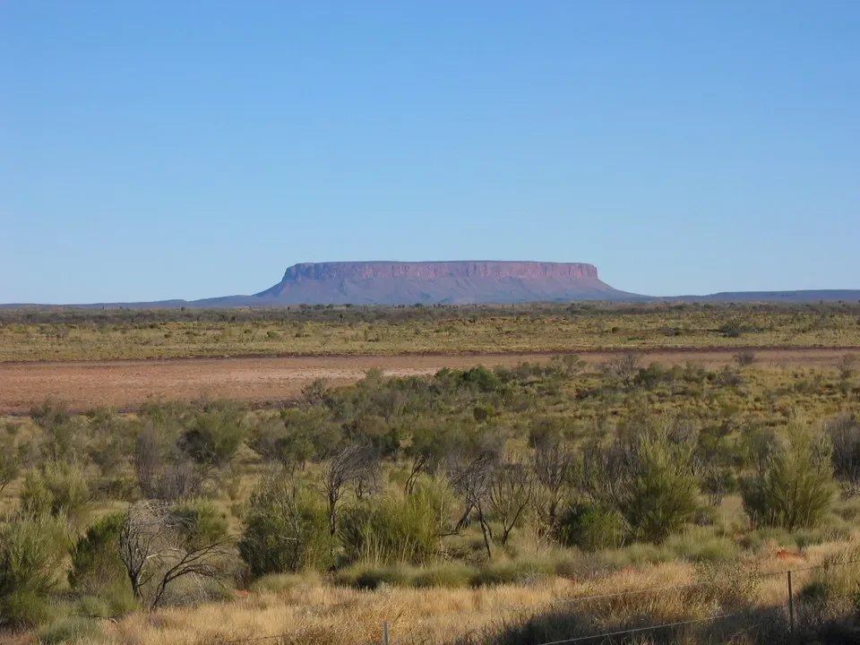 Paesaggio del deserto australiano con una formazione rocciosa all'orizzonte.