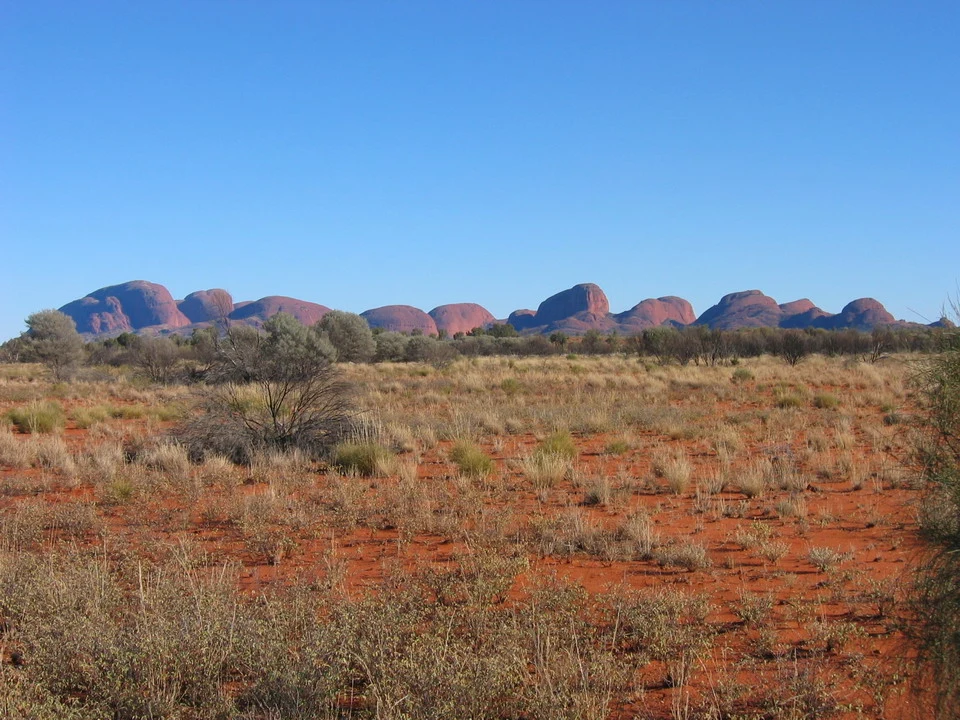 Paesaggio arido australiano con formazioni rocciose rossastre all'orizzonte.