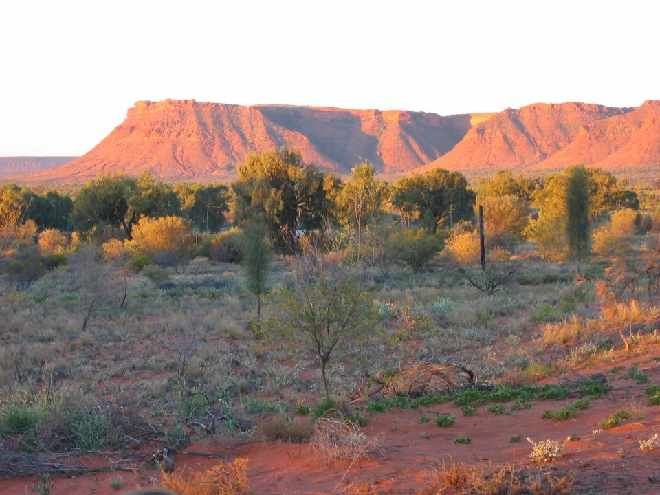 Paesaggio arido australiano con formazioni rocciose rosse al tramonto.