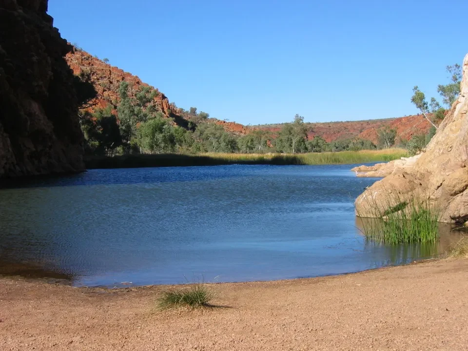 Un lago blu calmo circondato da formazioni rocciose rosse nell'entroterra australiano.