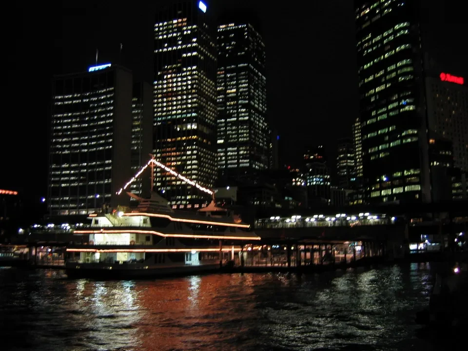 Paesaggio notturno del centro di Sydney con edifici alti e un traghetto sul fiume.