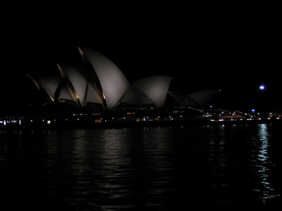 La Sydney Opera House illuminata di notte si riflette sull'acqua.