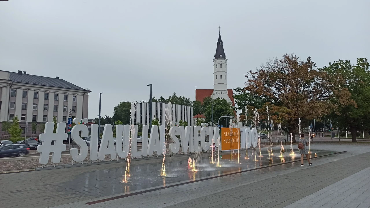 Una piazza con fontane e un edificio storico in stile baltico sotto un cielo grigio.