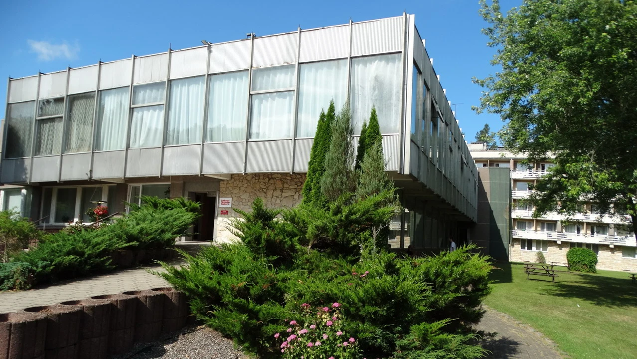 Vista esterna di un edificio moderno con ampie finestre e vegetazione in primo piano.
