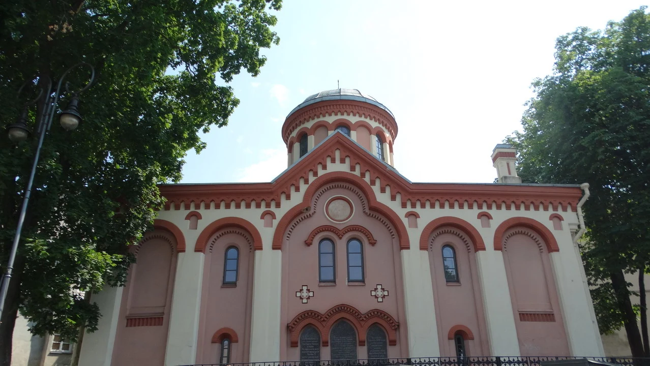 Facciata di una chiesa ortodossa rosa e bianca incorniciata dagli alberi.