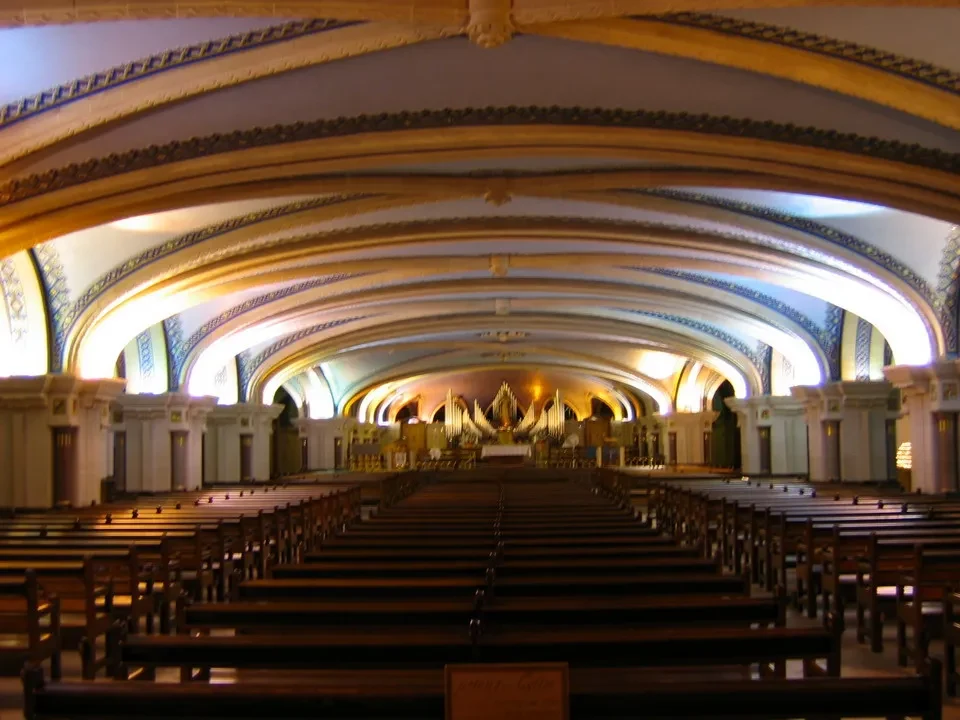 Interno di una navata di una chiesa con file di sedie in legno che si estendono verso l'orizzonte.