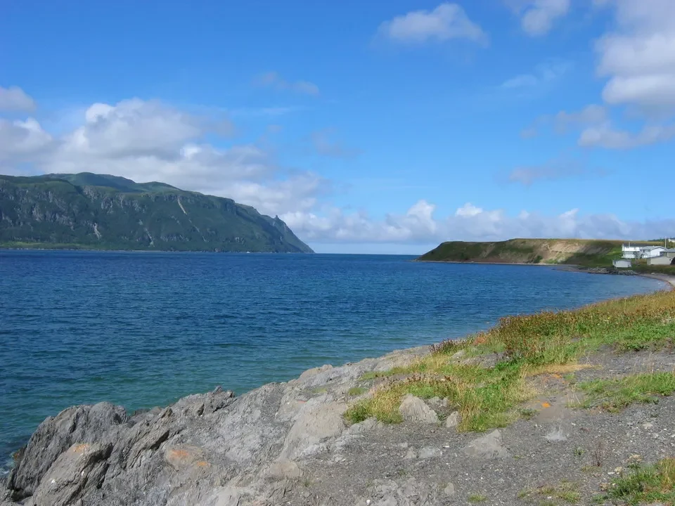Paesaggio costiero con acqua blu e scogliere rocciose sotto un cielo nuvoloso.