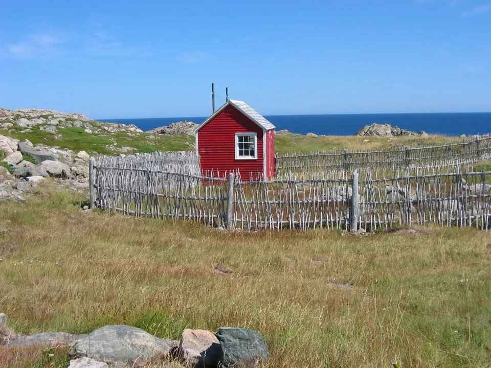 Una piccola casa rossa è circondata da una staccionata in un paesaggio costiero canadese.