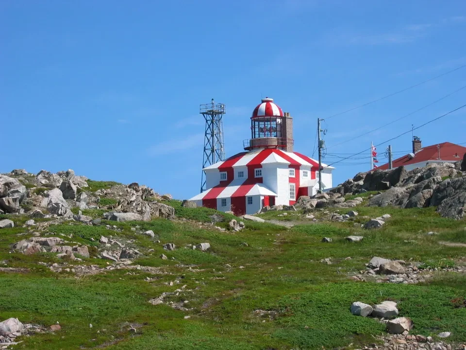 Un faro rosso e bianco sorge su una collina erbosa nel paesaggio canadese.