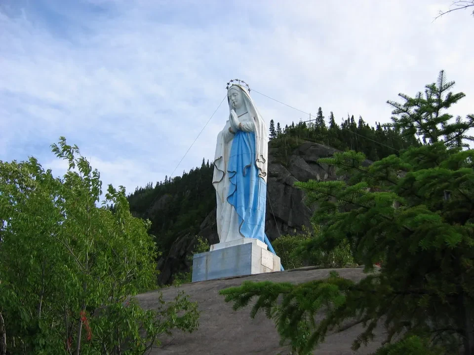 Statua della Vergine Maria su un promontorio roccioso e boscoso.