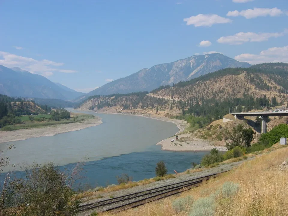 Paesaggio fluviale con montagne e una linea ferroviaria in Canada Occidentale.