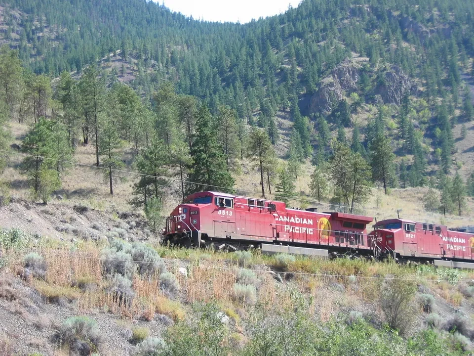 Un treno rosso attraversa un paesaggio boscoso in Canada Occidentale.