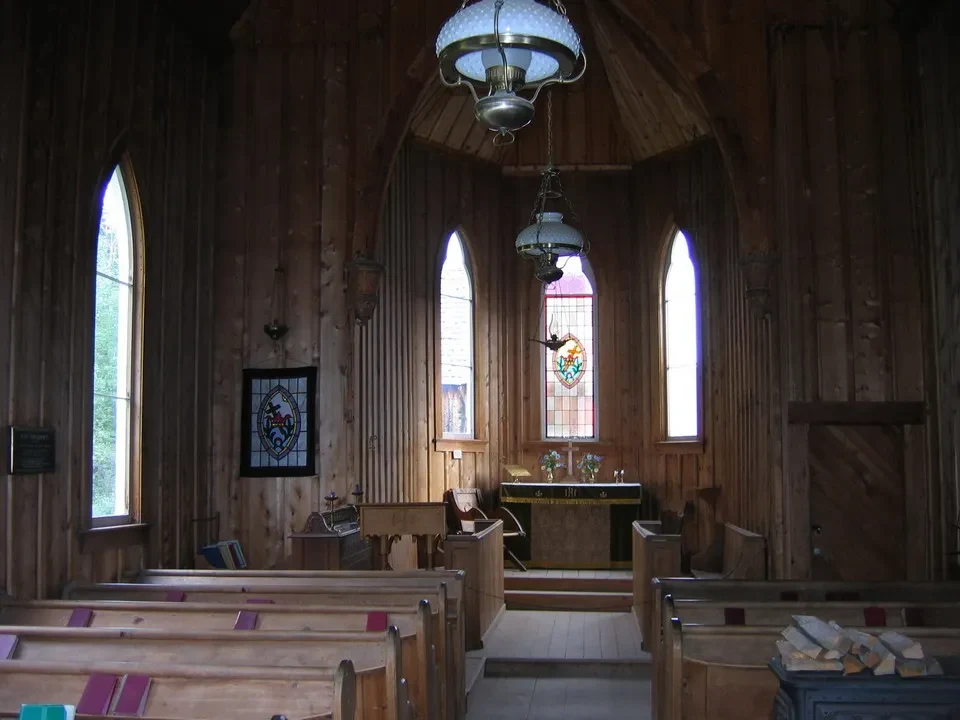 Interno di una chiesa in legno con banchi e finestre alte.