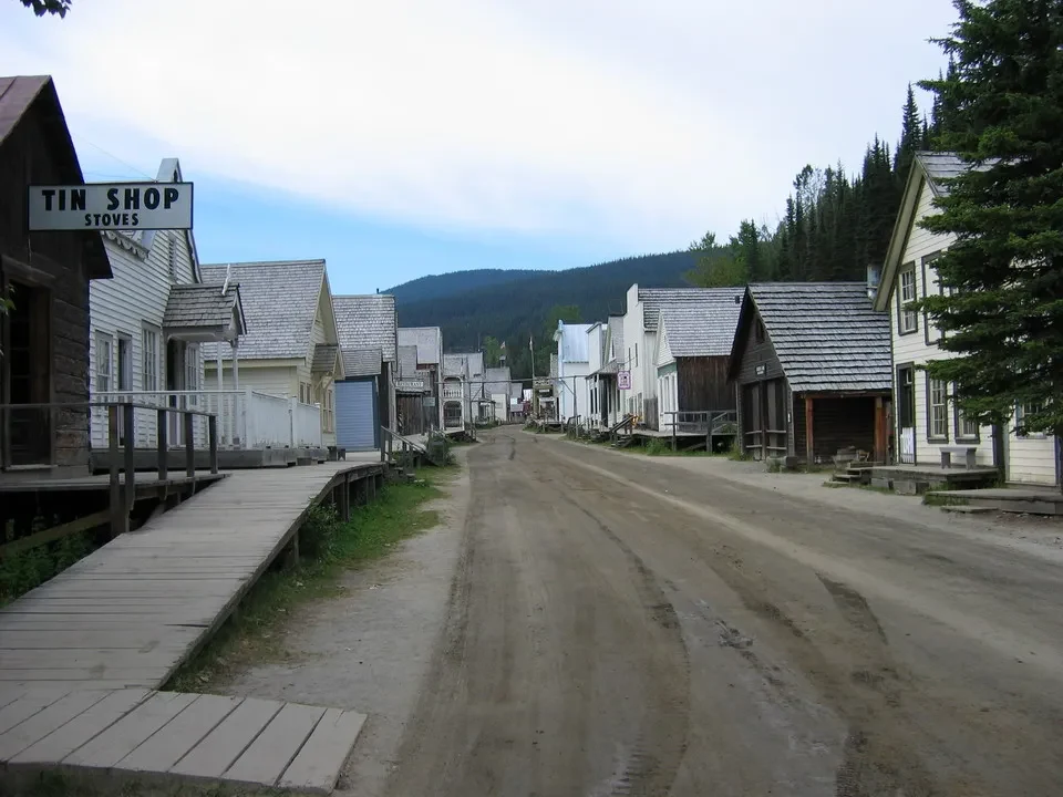 Una strada sterrata attraversa un villaggio di legno con edifici lungo i lati.