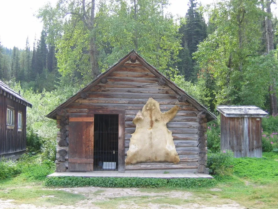 Un rustico edificio in legno con una scultura chiara appoggiata davanti, immerso nel verde boschivo.