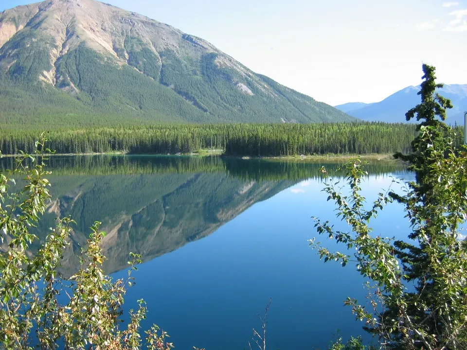 Un lago calmo riflette montagne boscose e alberi fitti.