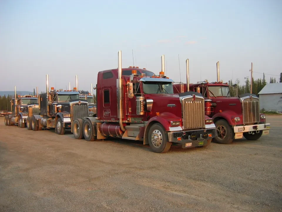 Una fila di camion rossi è parcheggiata su una strada sterrata all'alba in Canada Occidentale.