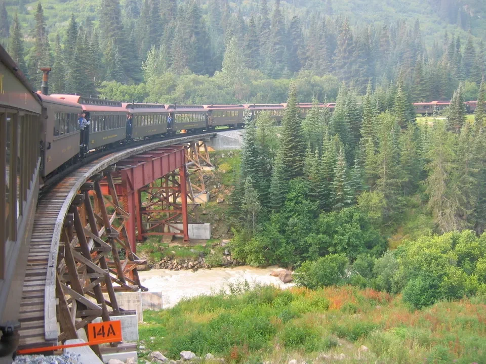 Treno rosso attraversa un ponte ligneo in una valle boscosa in Canada Occidentale.