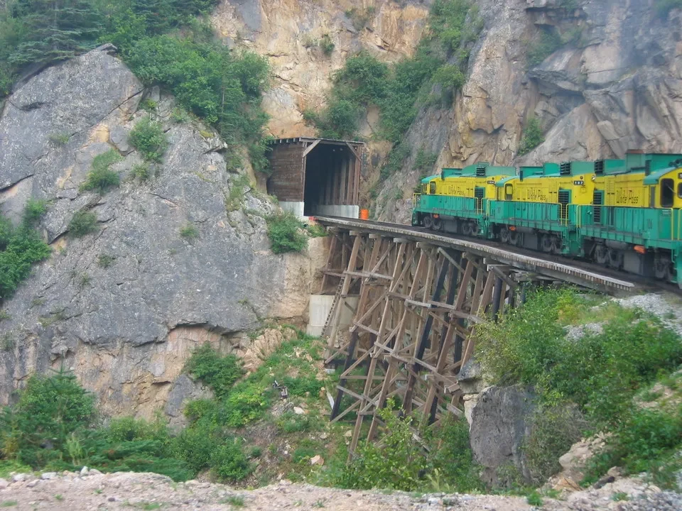 Treno verde attraversa un ponte ligneo sopra una gola rocciosa in Canada occidentale.