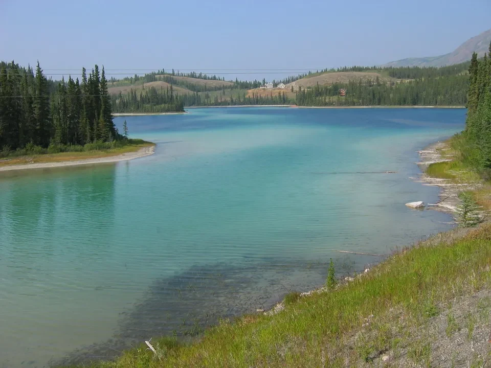 Un lago turchese circondato da vegetazione verde e colline erbose.