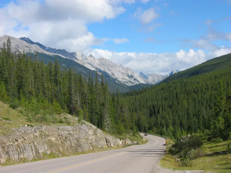 Una strada asfaltata serpeggia attraverso un paesaggio montano boscoso in Canada Occidentale.