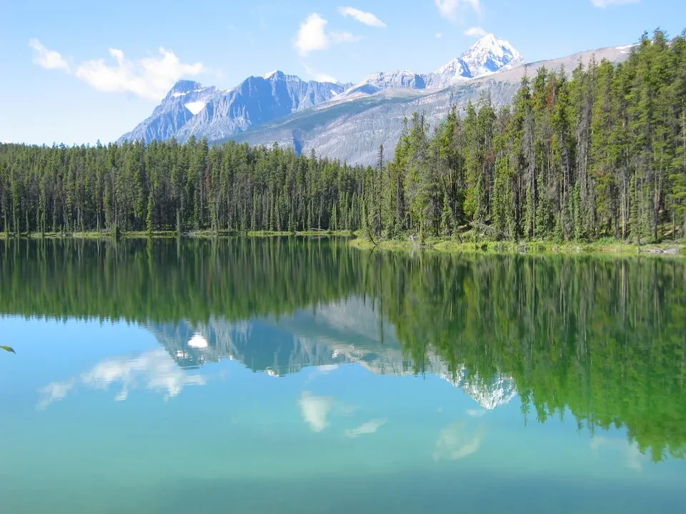 Paesaggio alpino con un lago e foreste boscose riflette le montagne innevate.