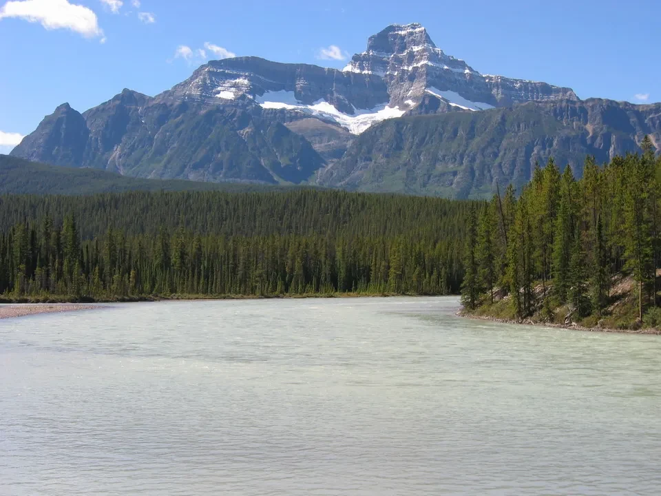 Un fiume ampio scorre attraverso una valle boscosa con montagne innevate sullo sfondo.