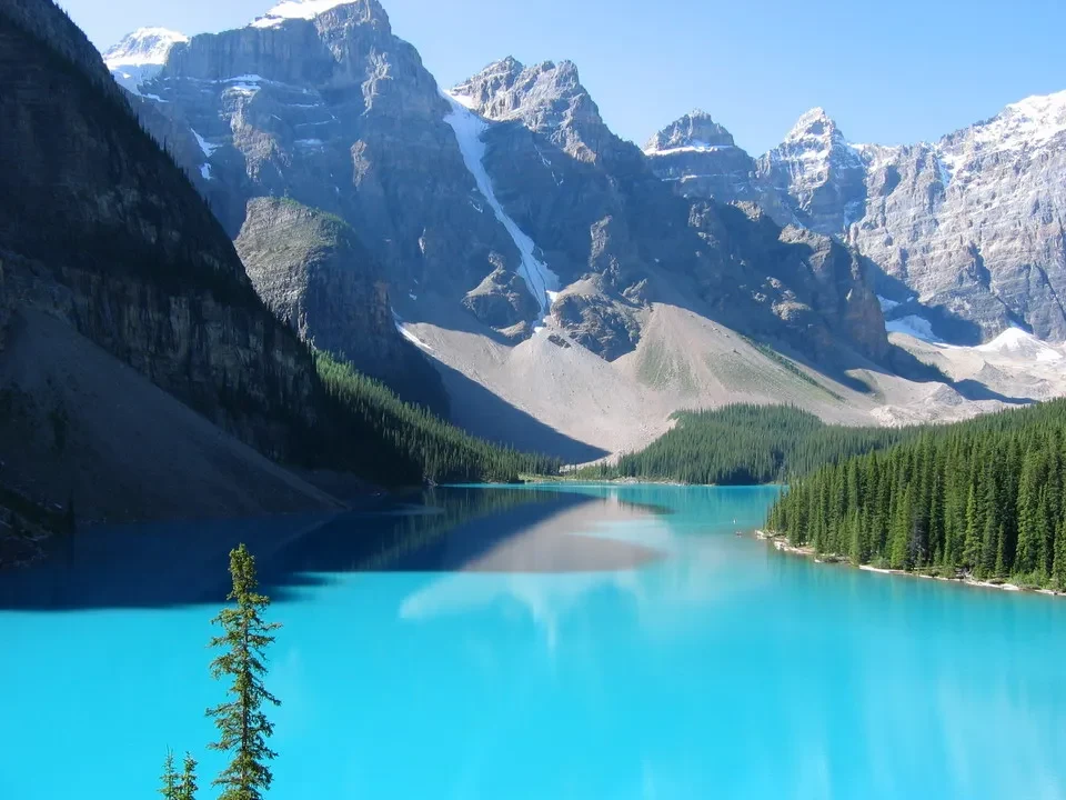 Lago turchese alpino circondato da montagne rocciose e foreste verdi.