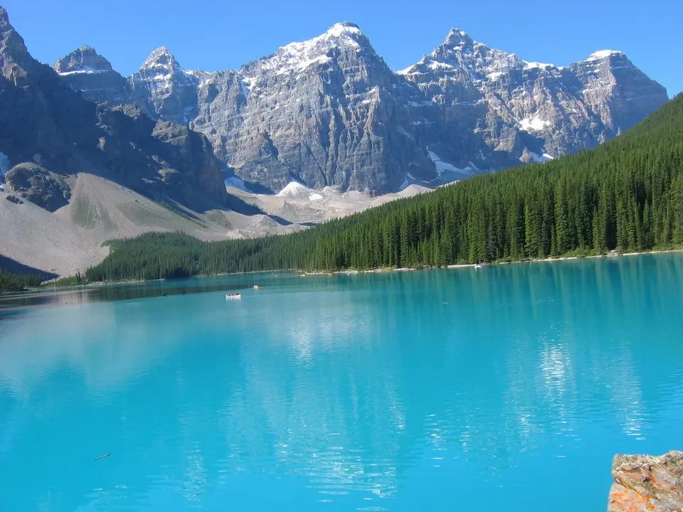 Un lago turchese circondato da montagne innevate e foreste verdi.