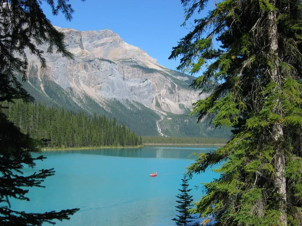 Un lago turchese si estende tra montagne rocciose e foreste di conifere.