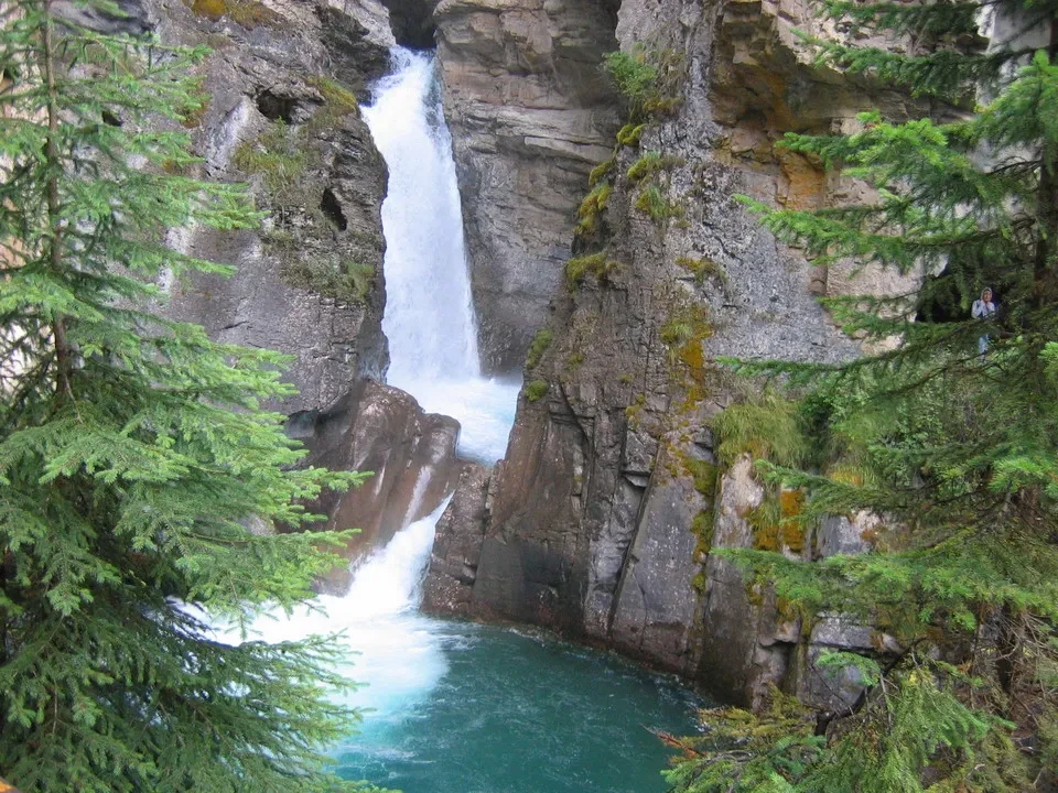 Una maestosa cascata scende su pareti rocciose verso una pozza turchese verde.